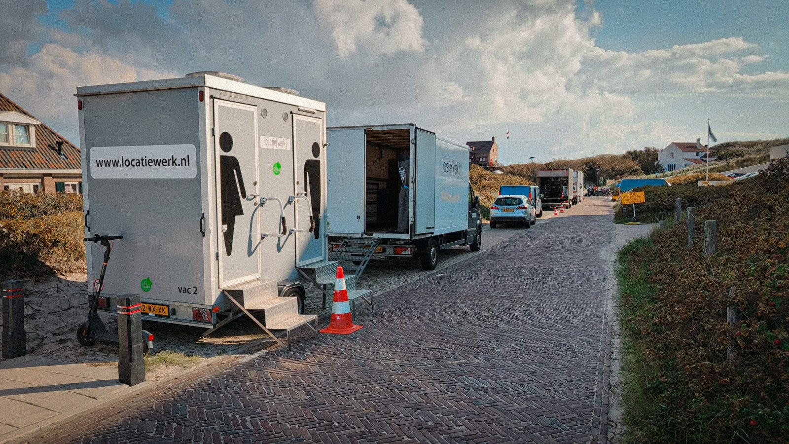 Toilet trailer and box trucks along a road in the dunes