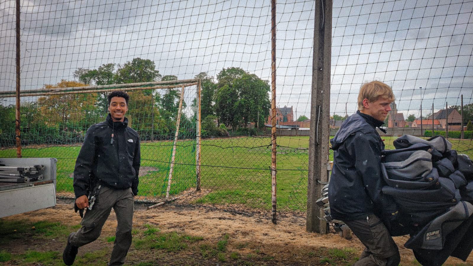 Crew carrying gear past a football pitch