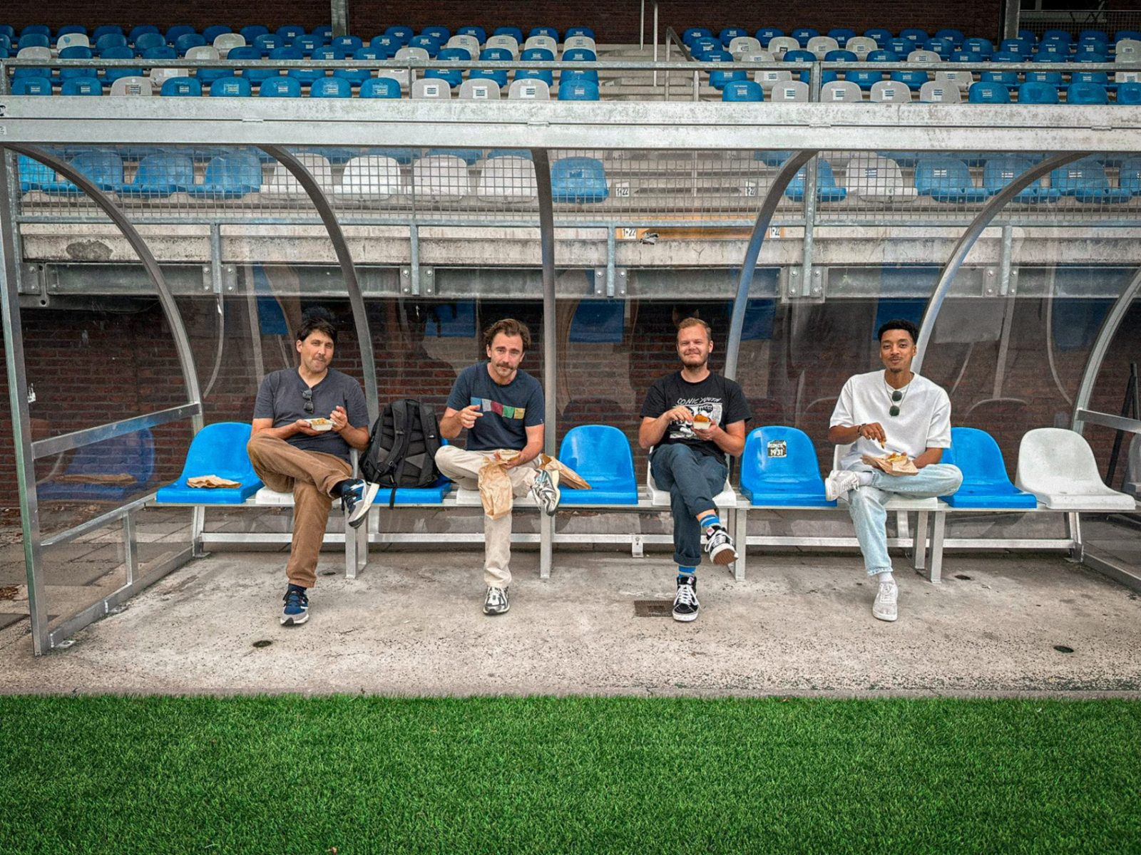 Crew eating together in the dugout of a sports ground